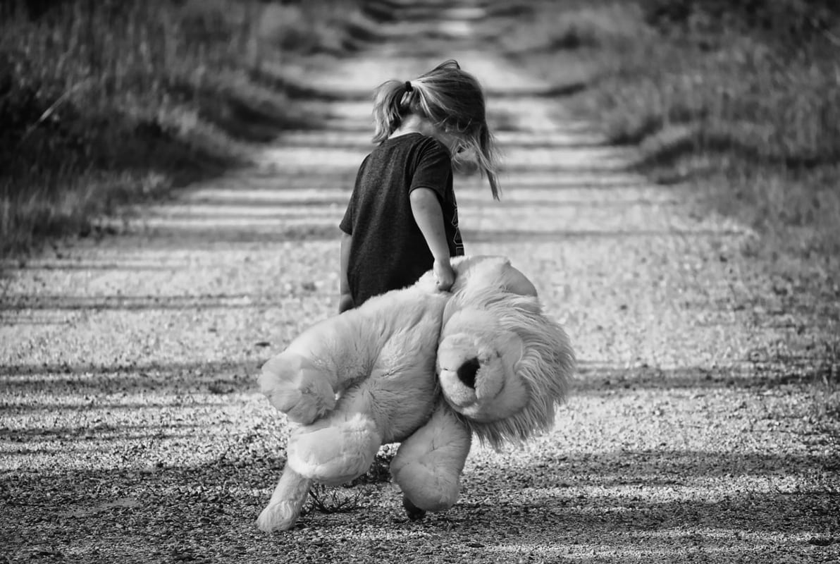 Black & White picture of child walking down road with stuffed toy