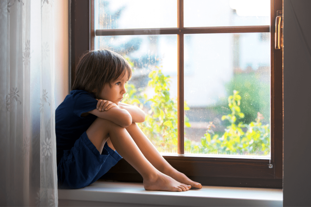 a sad boy sitting in a window